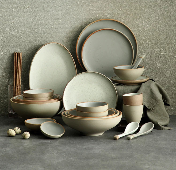 Set of ceramic dishes and tableware on a gray surface with a textured gray wall background.