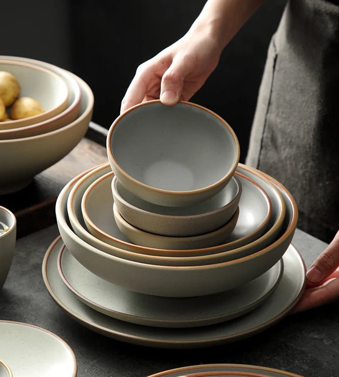 Stack of ceramic bowls and plates on a dark surface with a hand holding one of the bowls.