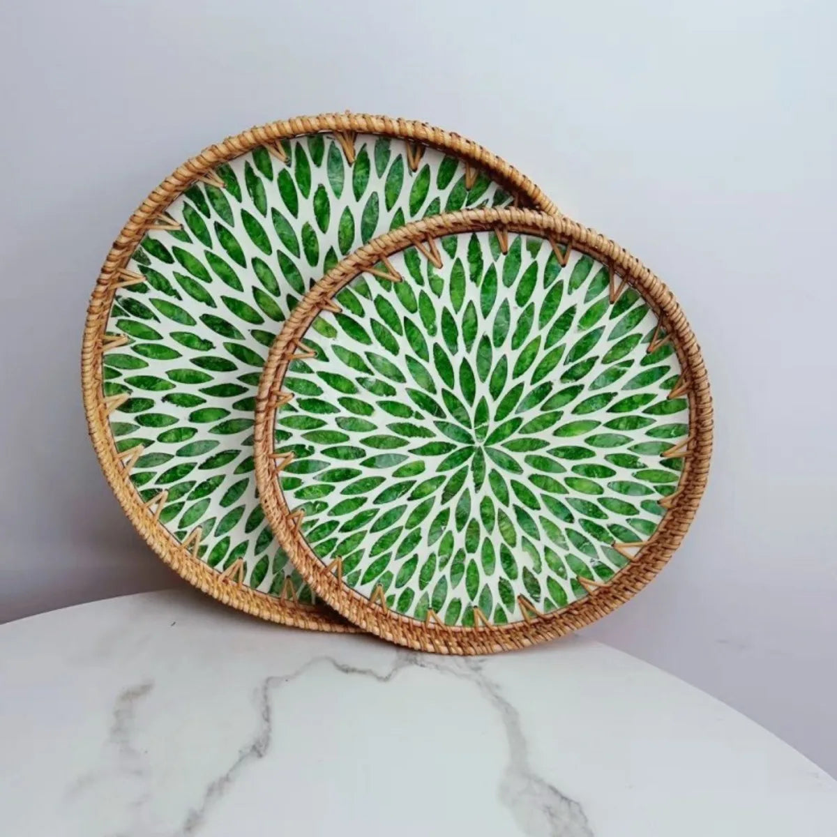 Two round woven coasters with green leaf pattern on a marble surface.