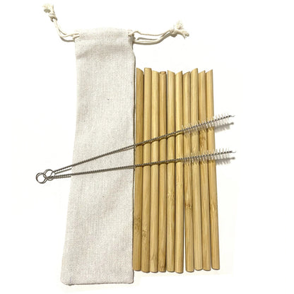 A clear glass filled with whole bamboo straws on a kitchen countertop with a marble background, beside an open notebook.
